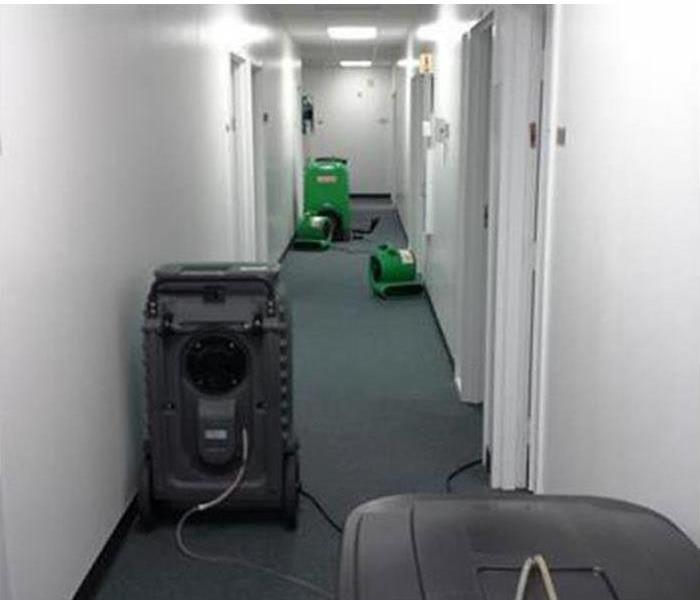 There is a hallway and there are three humidifiers and two air mover drying up the carpet on the hallway